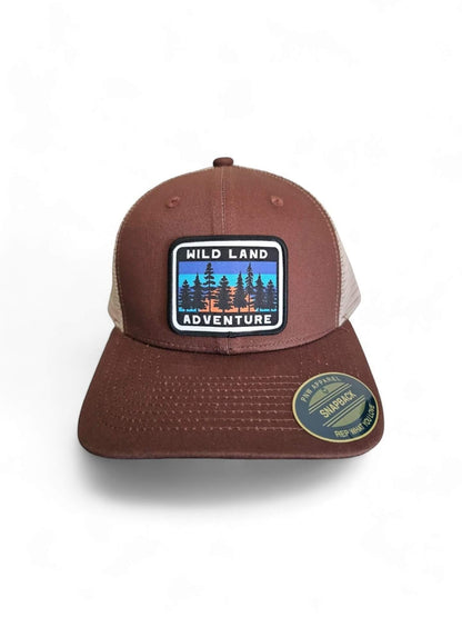 Moove Headwear brown trucker hat with mesh back and "Wild Land Adventure" patch featuring trees and sunset.