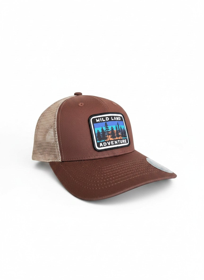 Moove Headwear brown trucker hat with mesh back and "Wild Land Adventure" patch featuring trees and sunset.