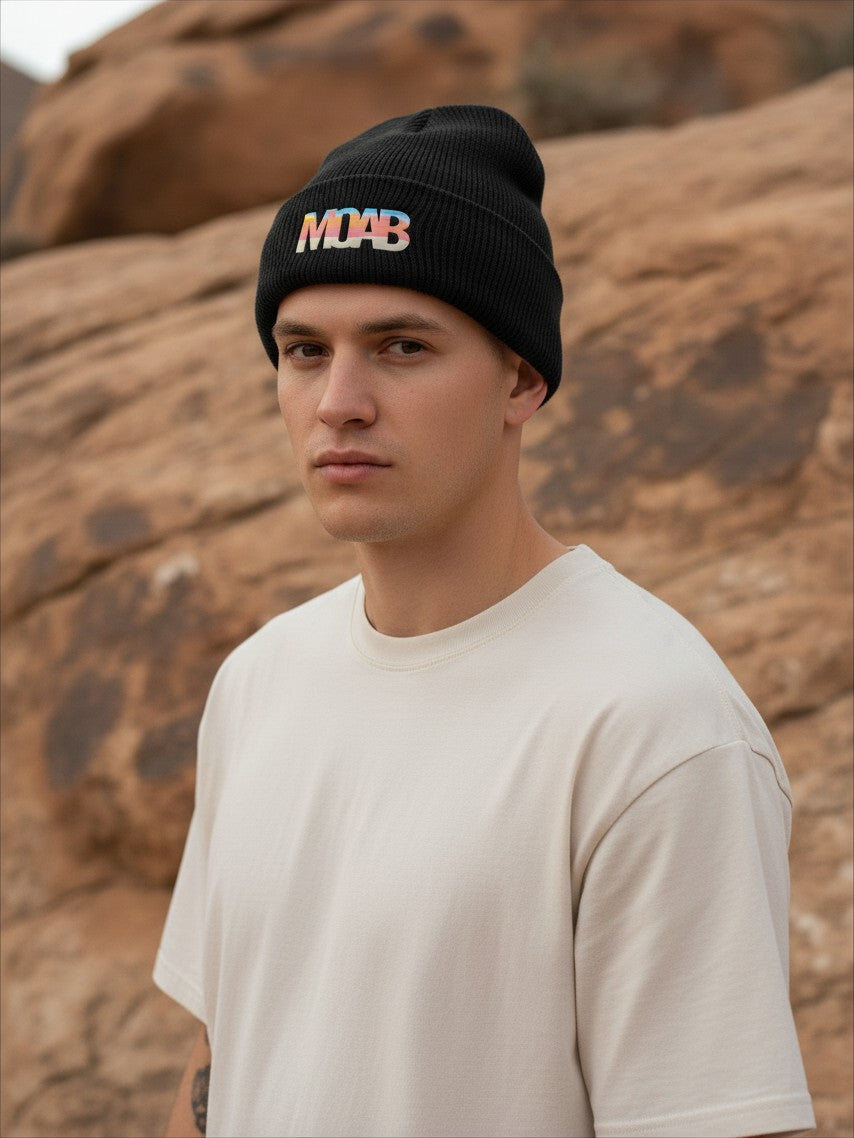 Moove Headwear black rib-knit beanie with a colorful Moab sunset patch worn by a man in a desert landscape