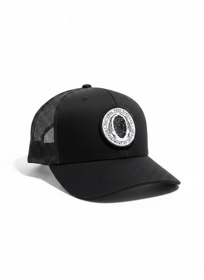 Moove Headwear black trucker hat with National Park Service Sequoia Cone embroidered patch, mesh back, and snapback closure.