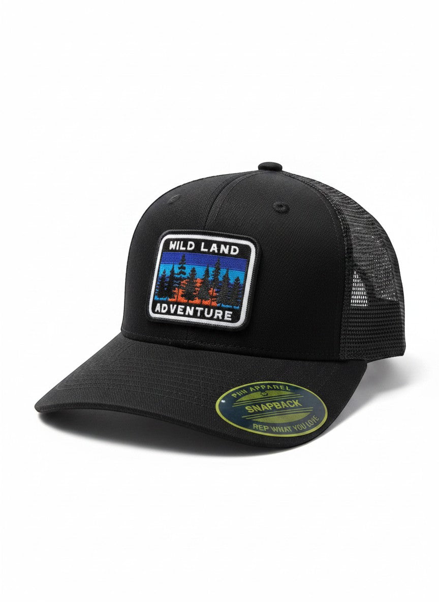 Moove Headwear black trucker hat with mesh back and a "Wild Land Adventure" patch featuring trees and a sunset.