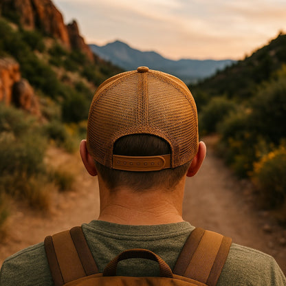 Moove Headwear brown trucker hat with mesh back and snapback closure, worn by a person with a backpack on a trail.