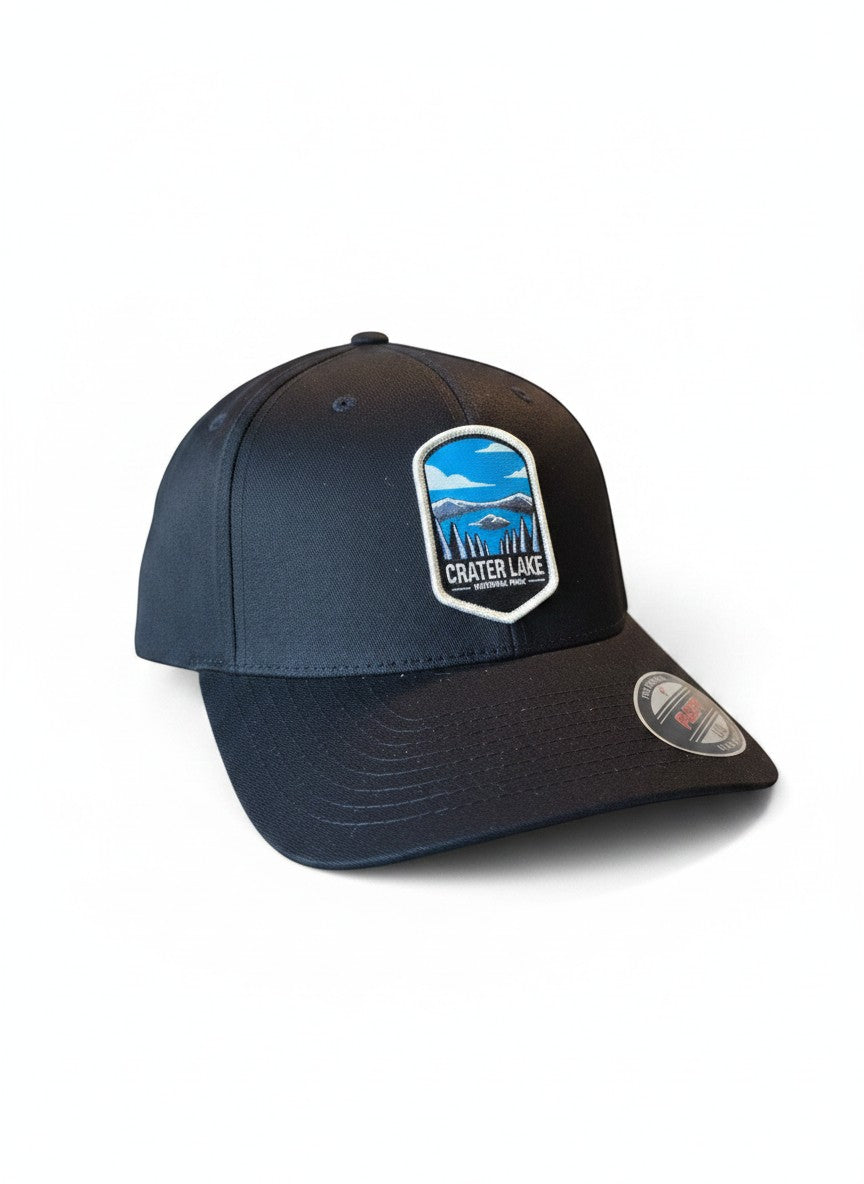 Moove Headwear black Flexfit cap with embroidered Crater Lake National Park patch featuring lake, mountains, and trees.