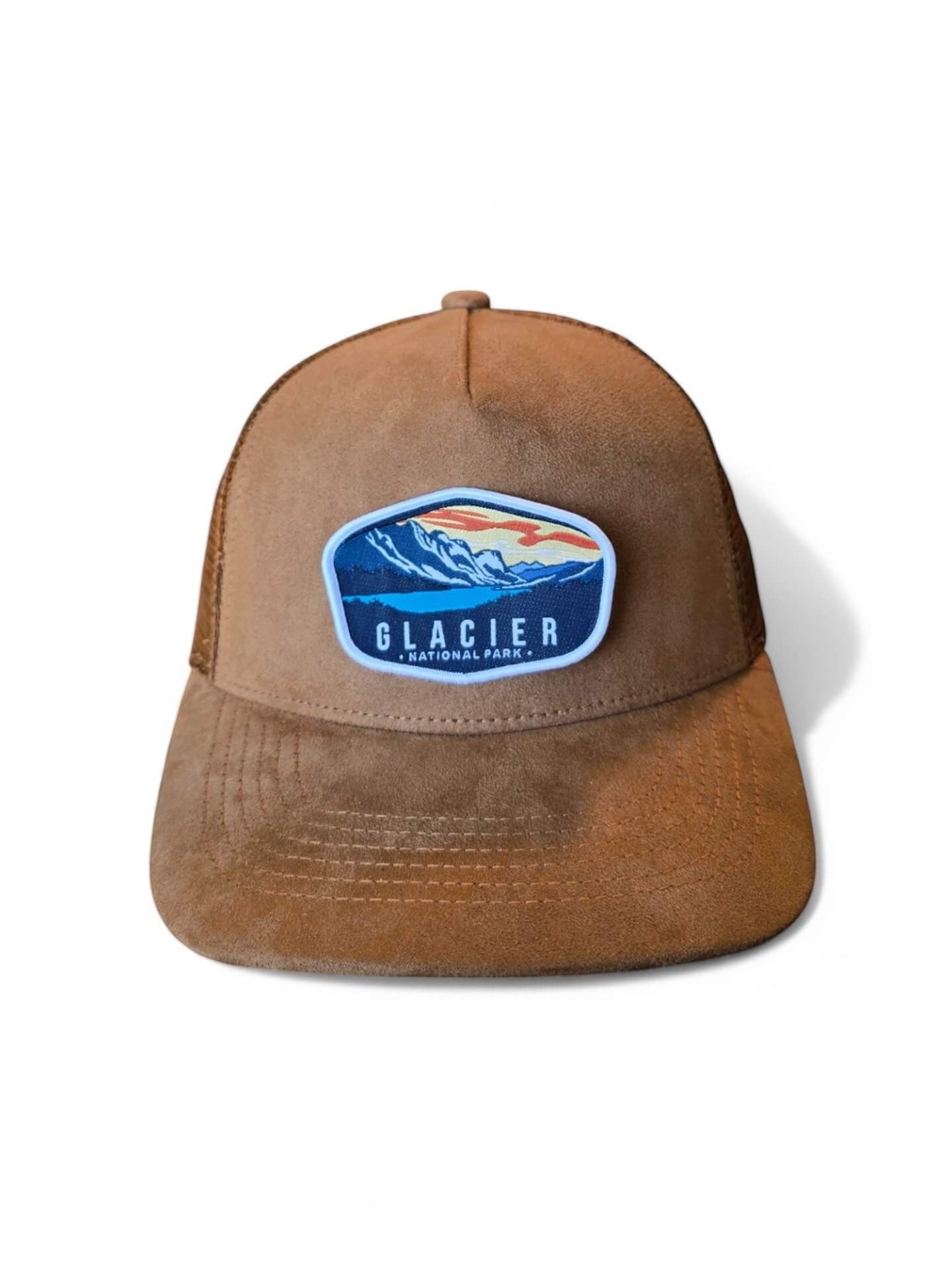 Moove Headwear brown suede trucker hat with embroidered Glacier National Park patch, mesh back, and 5-panel construction.