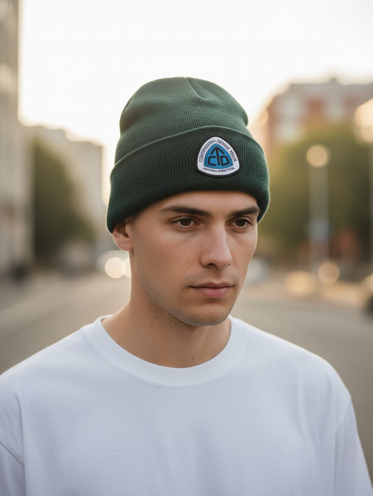 A man wearing a dark green Moove Headwear Continental Divide Trail beanie with a branded patch in an urban setting.