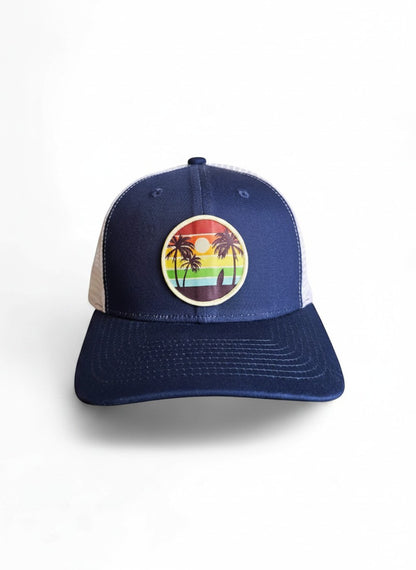 Moove Headwear navy blue trucker hat with mesh back and a circular patch featuring palm trees and a sunset.