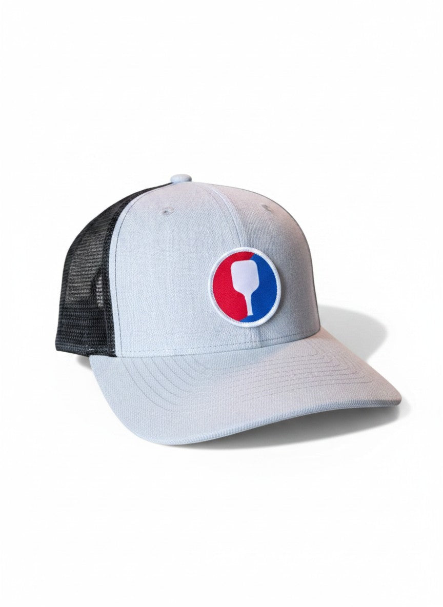 Moove Headwear light grey trucker hat with black mesh back and a circular pickleball paddle patch.