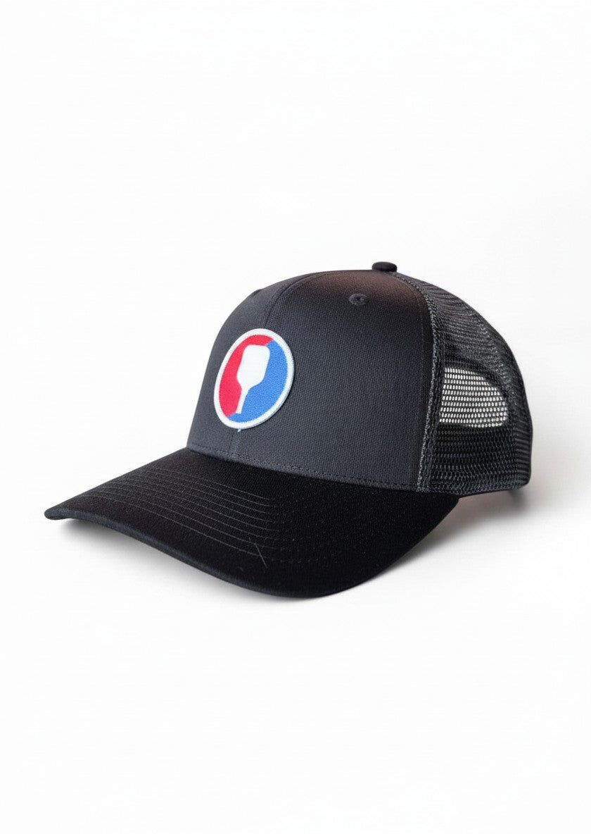 Moove Headwear dark grey trucker hat with black brim and pickleball paddle patch. Mesh back.