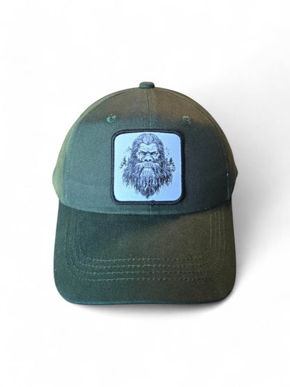 Moove Headwear dark green dad hat with a woven patch featuring a sketch of Bigfoot and trees.