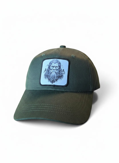 Moove Headwear dark green dad hat with a woven patch featuring a sketch of Sasquatch's face and trees.