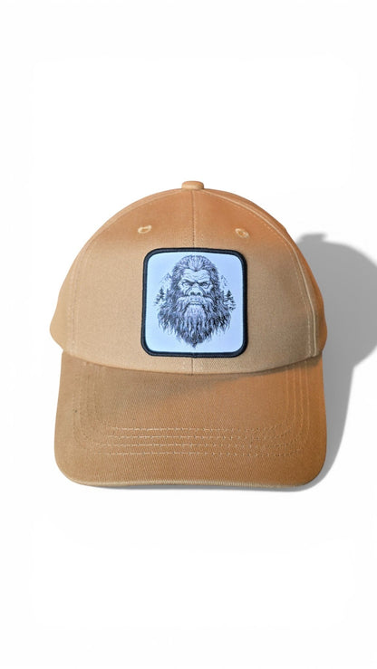 Moove Headwear tan dad hat with a woven patch featuring a black and white illustration of Sasquatch and pine trees.