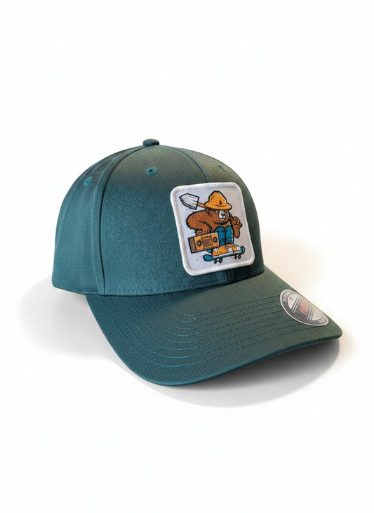 Moove Headwear teal Flexfit hat with Smokey Bear skateboarding patch. Features a mid-profile crown and stretch-fit comfort.