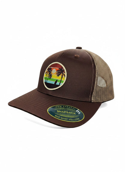 Moove Headwear brown trucker hat with mesh back and a circular patch featuring palm trees, a surfboard, and a rainbow sunset.